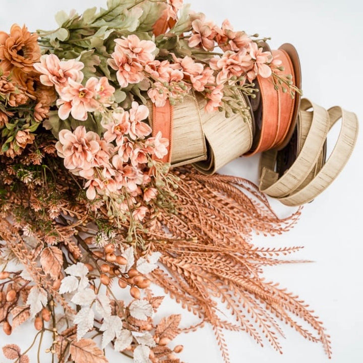 A styled flat-lay of dried floral arrangements and a spool of wavy tan ribbon on a white background.