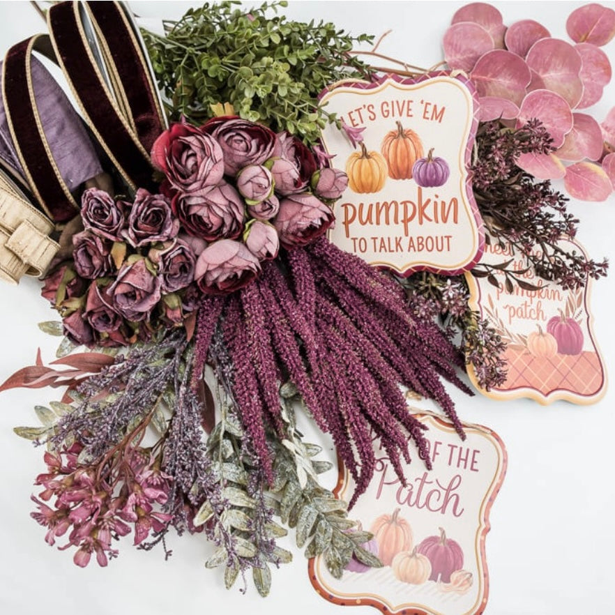 A styled autumn floral arrangement and sign set on a white background, featuring mauve and burgundy faux roses, purple seed heads, green foliage, pink decorative leaves, velvet ribbon, and three decorative signs reading phrases like 'Let's Give 'em Pumpkin to Talk About' and 'Pumpkin Patch.'.