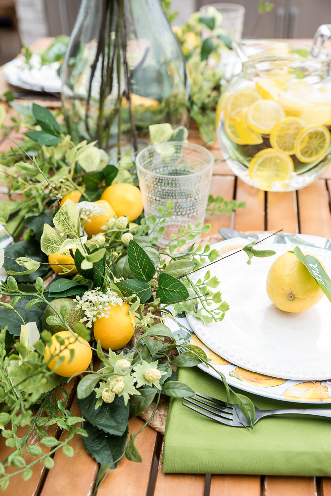 Decorative table setting with lemons, greenery, and plates on a wooden table.