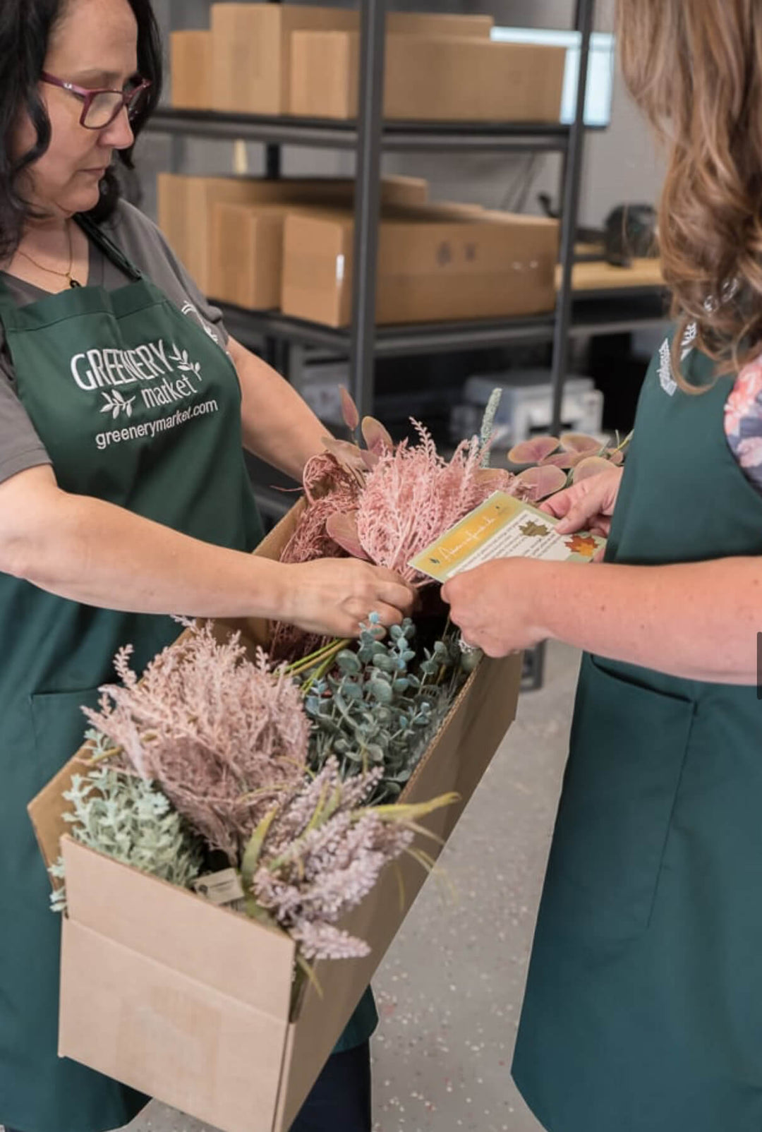 Two people in green aprons working with flowers in a warehouse setting.